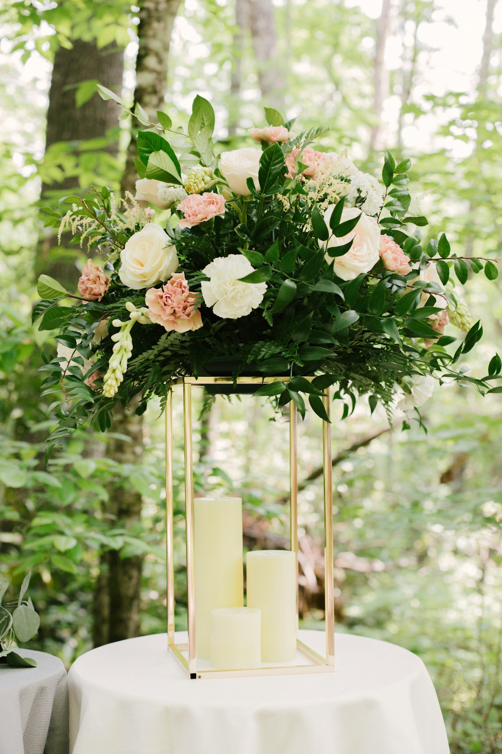 White and blush roses on a gold frame stand with pillar candles glowing inside