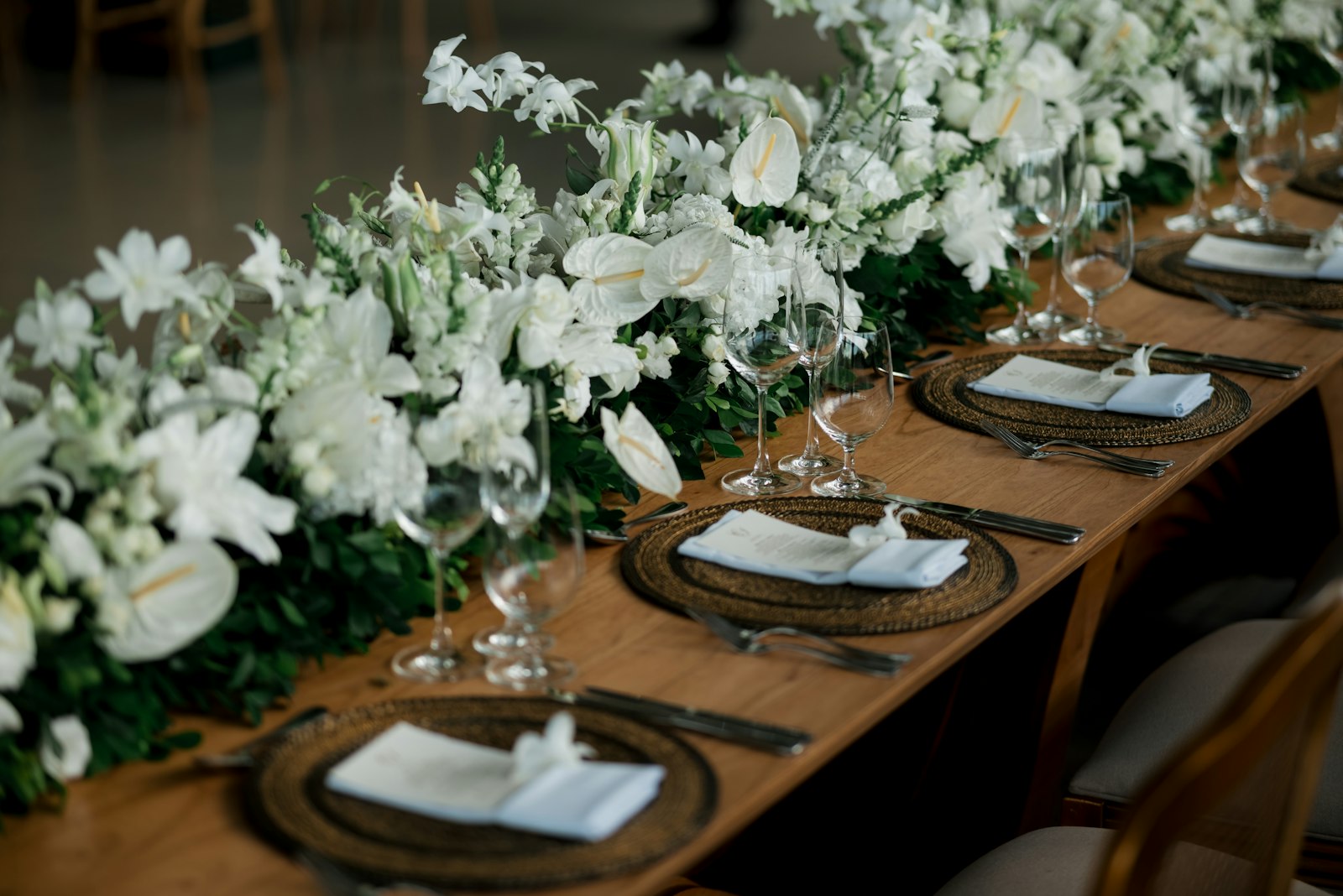 Lush white floral runner down a wooden banquet table set with rattan chargers