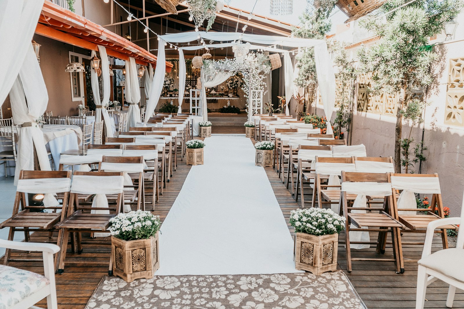 Ceremony space with white fabric draped overhead, a white aisle runner and white florals in wooden boxes