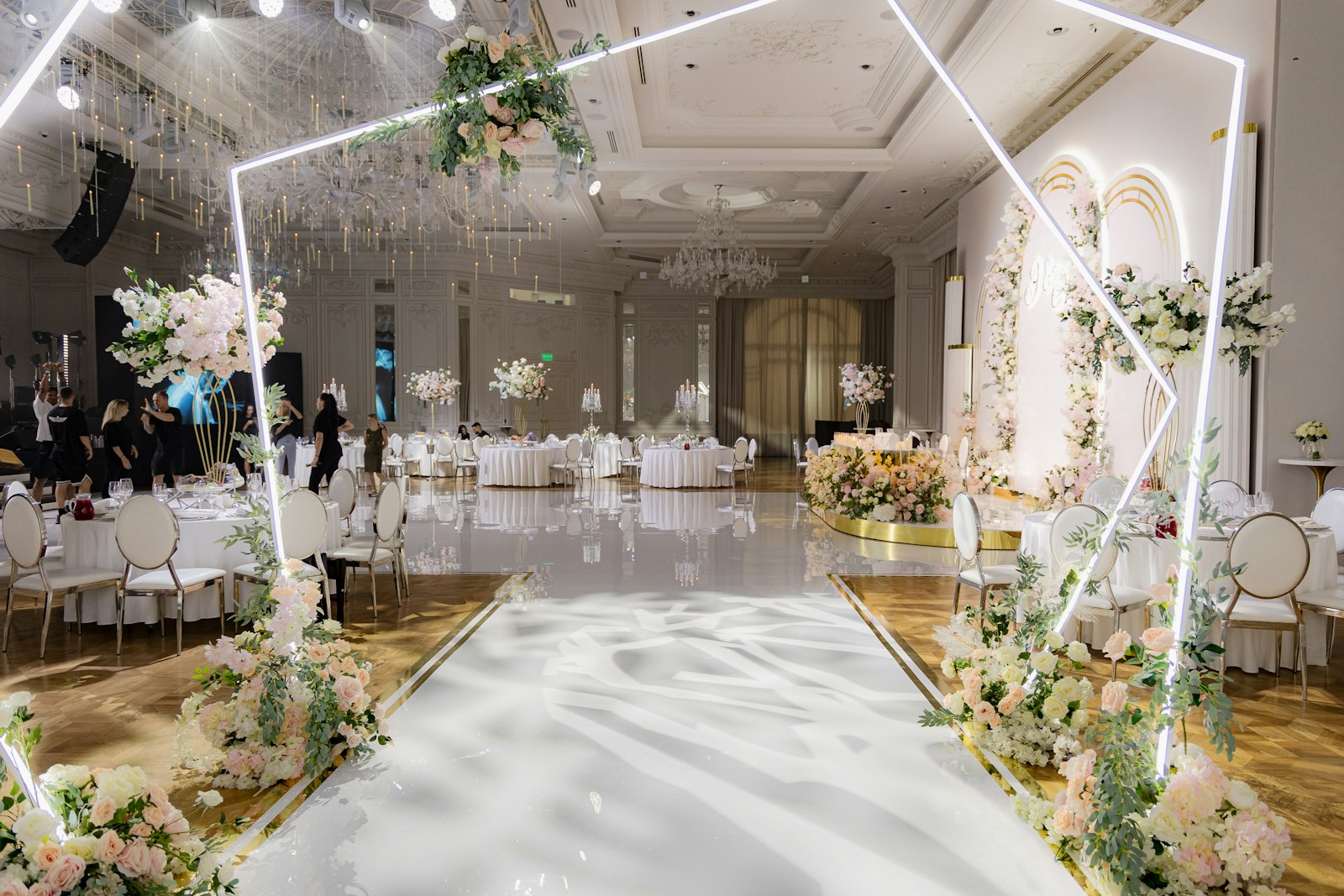 Ballroom ceremony with a white neon hexagon arch over a mirrored aisle lined with blush and white flowers