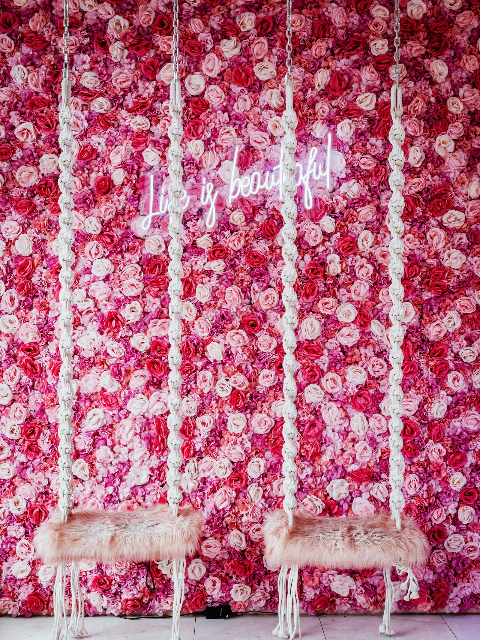 Pink flower wall with a white neon script sign and two macrame swing chairs