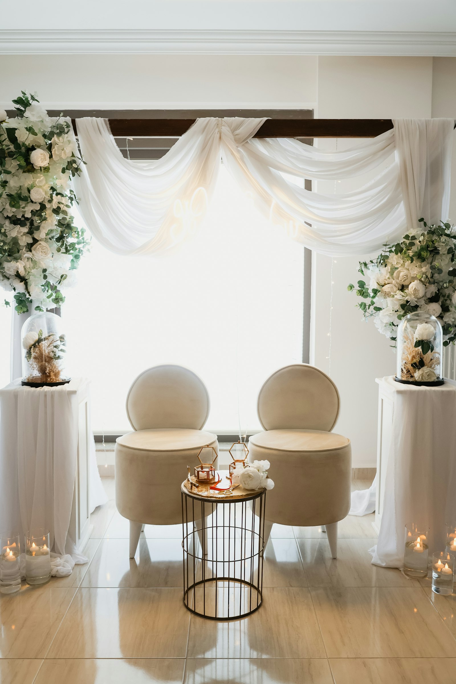 Ivory chiffon swag backdrop with white rose columns on plinths and two cream boucle chairs