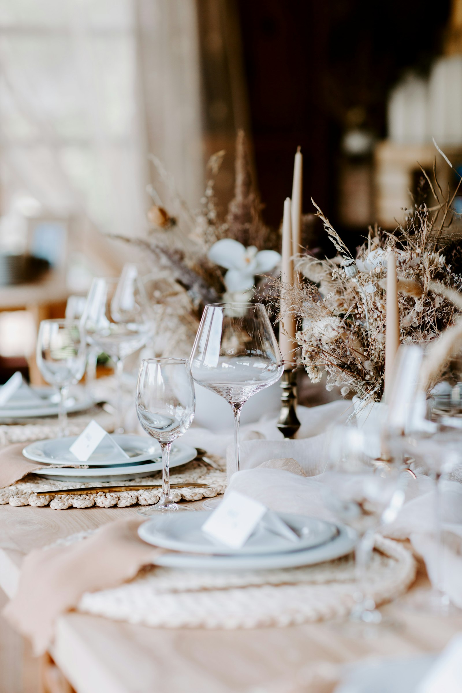 Boho tablescape with dried pampas grass, white orchids, tall taper candles and blush napkins on woven placemats