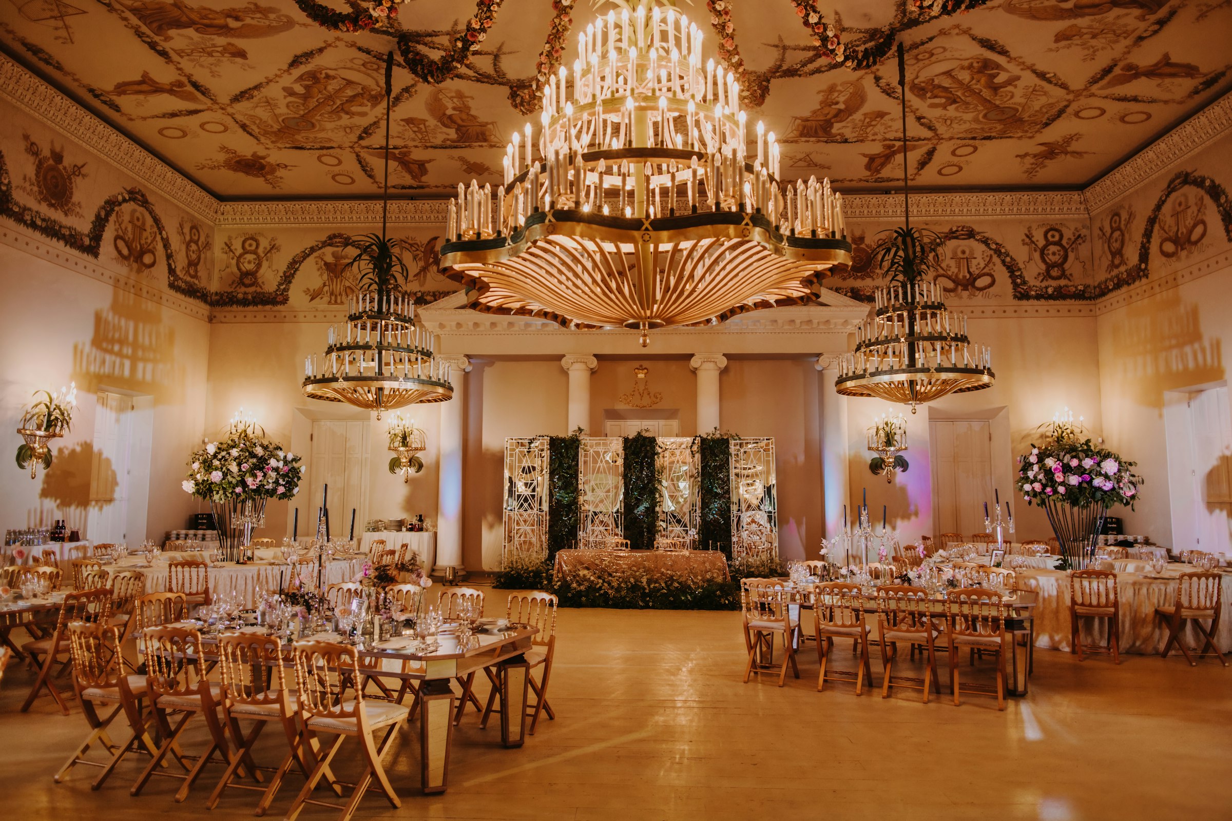 Grand ballroom with a frescoed ceiling, oversized crystal chandeliers and a greenery backdrop